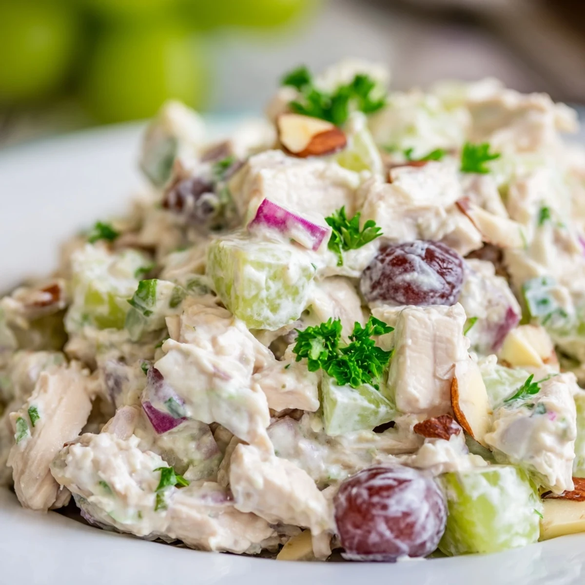 Scoop of creamy Chicken Salad with chopped celery, red onion, and halved grapes on a wooden serving platter.
