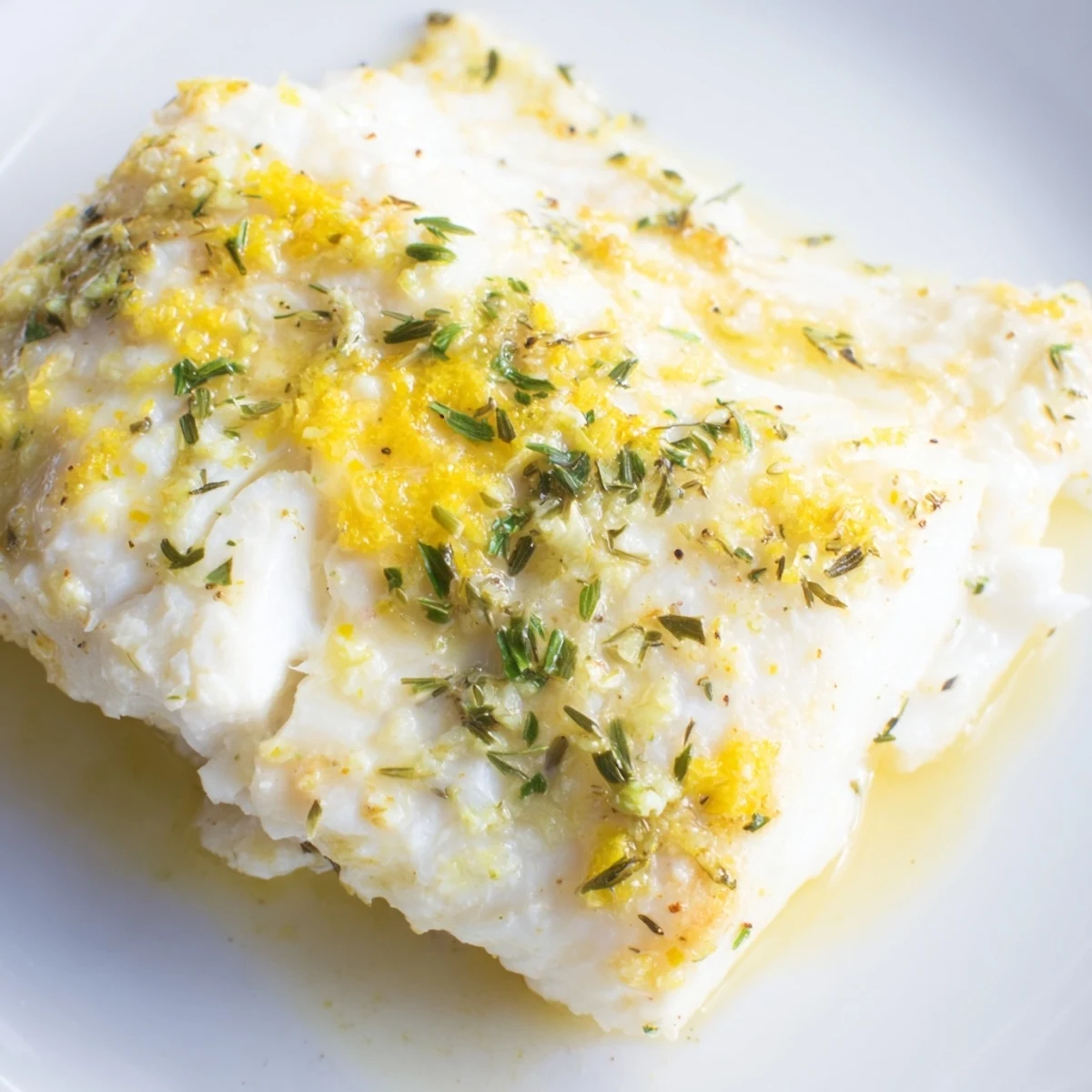 Flaky tender baked halibut fillet featuring a zesty lemon herb butter topping on a rustic plate.