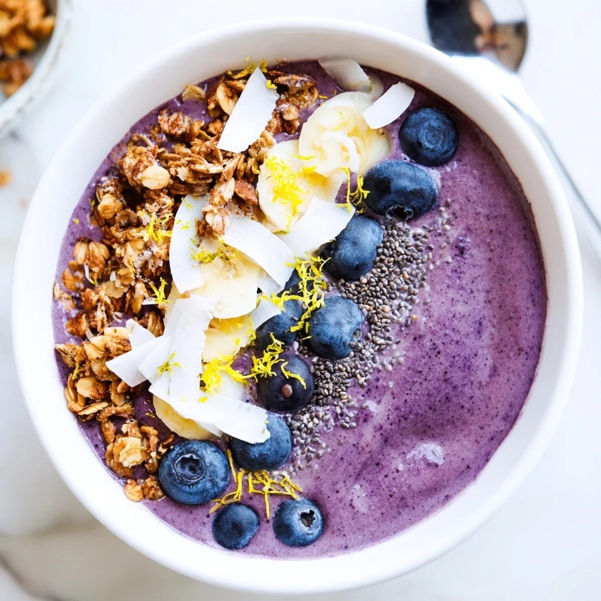 Bright purple Lemon Blueberry Smoothie Bowl with creamy texture and a crunchy granola topping in a white bowl.