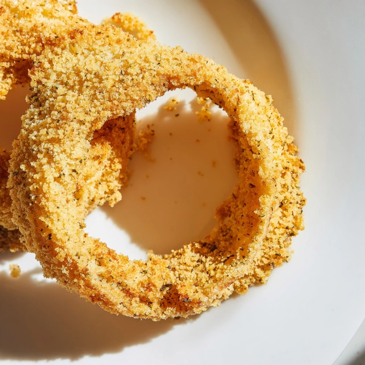 From the air fryer to the table, these Crispy Air Fryer Onion Rings shine with oil and spices, paired with fresh parsley garnish.