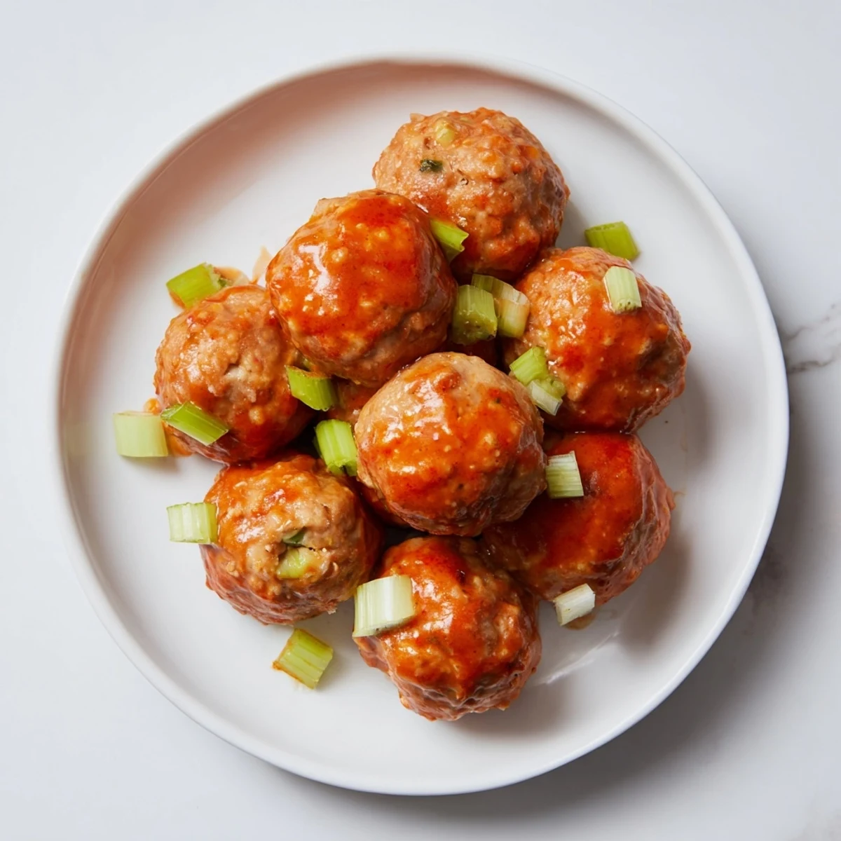 Golden-brown Touchdown Buffalo Chicken Meatballs coated in glossy, spicy red sauce are served on a platter with crisp celery and carrot sticks. 