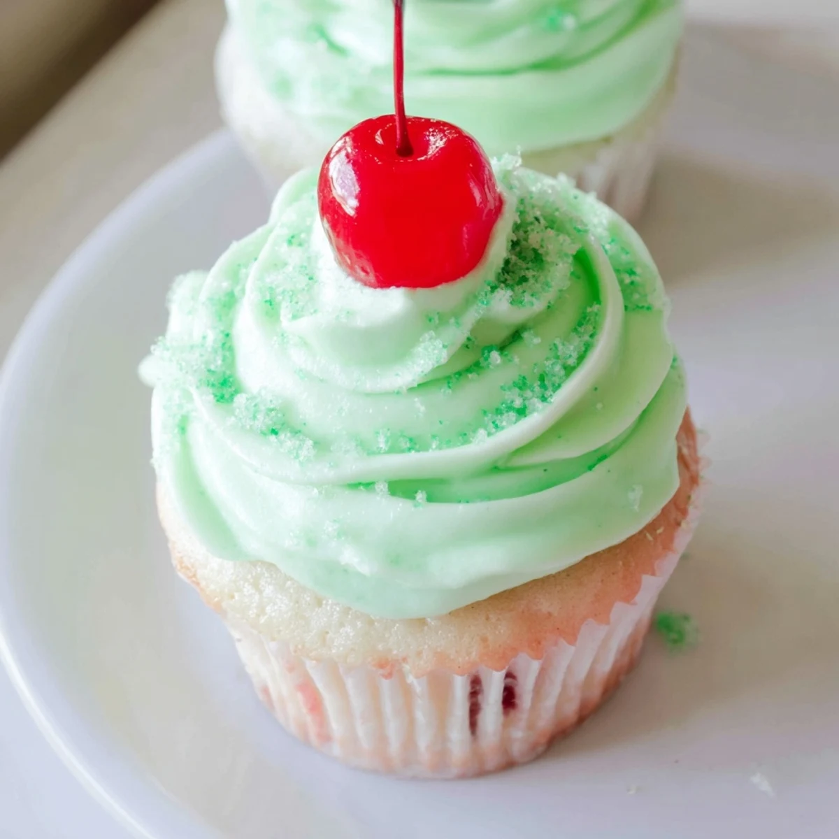 Freshly baked Shamrock Shake Cupcakes with mint frosting on a wooden board, with green sprinkles and a cherry on top. 