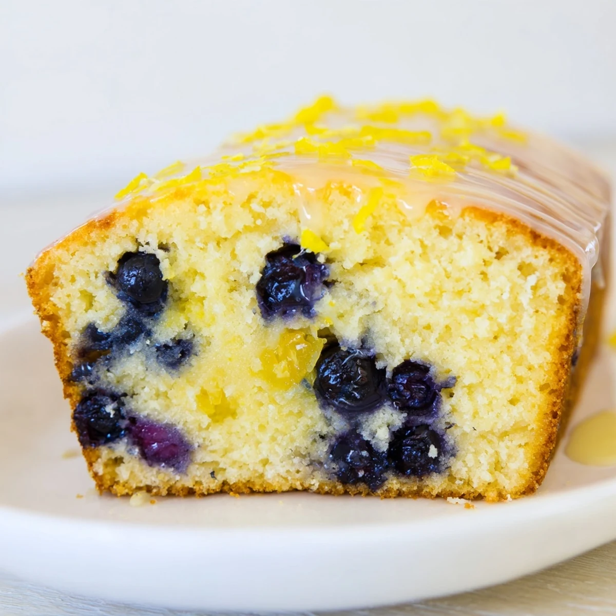 A close-up shot of a Lemon Blueberry Yogurt Loaf Cake, showcasing the tender, golden-brown crust and the burst of purple blueberries inside each slice.