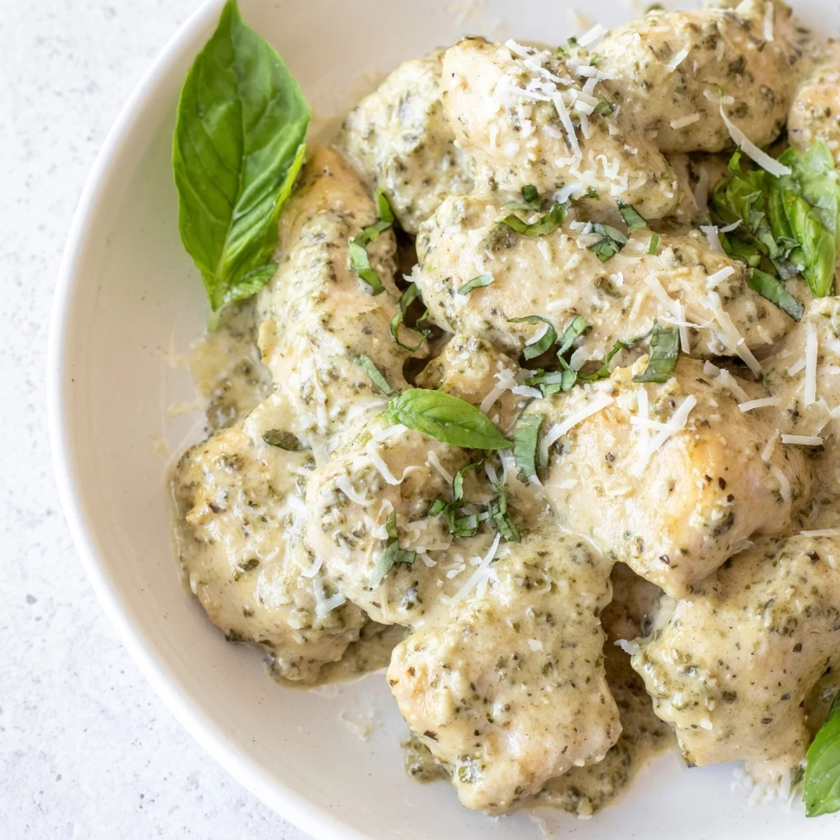 Slow cooker Pesto Ranch Crock Pot Chicken Thighs garnished with fresh basil and Parmesan.