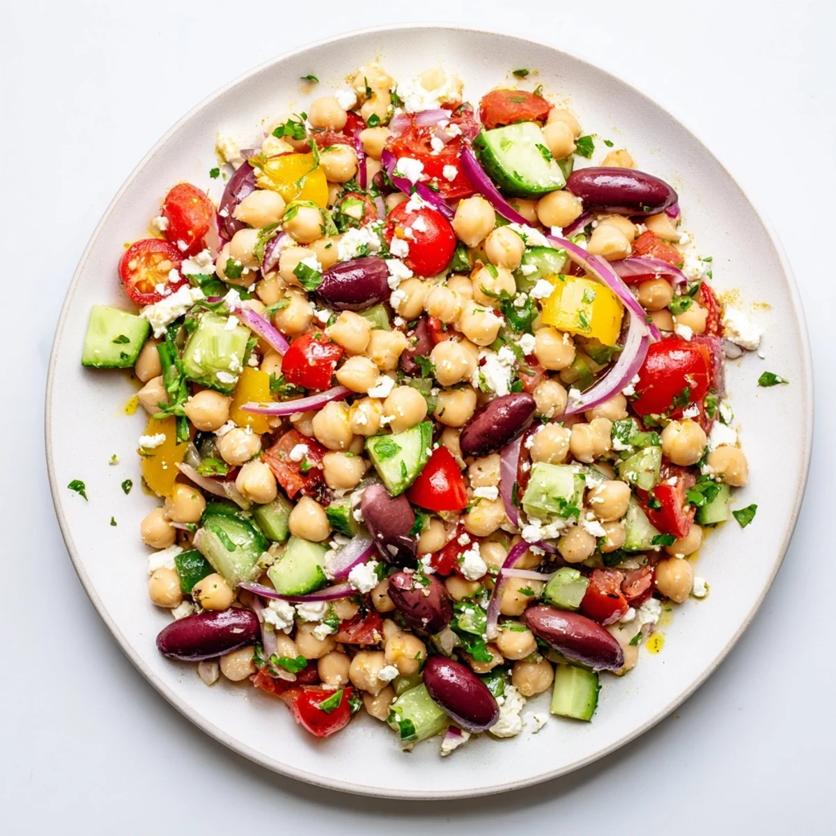 A close-up of Mediterranean Dense Bean Salad with chickpeas, tomatoes, and feta, glistening with olive oil and herbs.