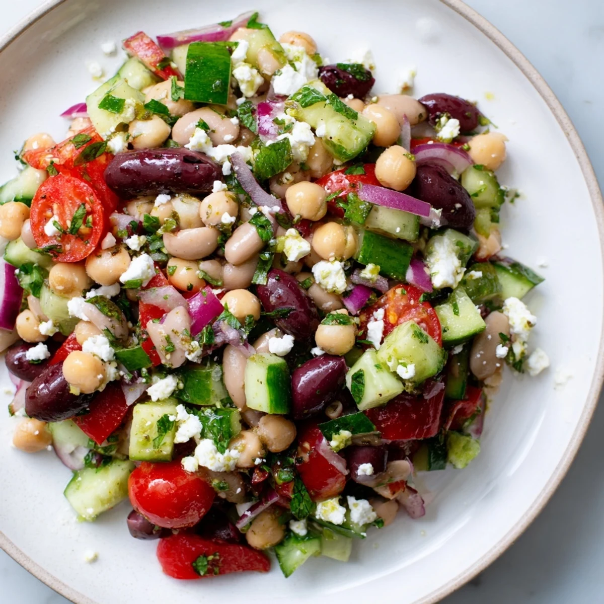 This vibrant Mediterranean Dense Bean Salad in a white bowl has fresh mint, olives, and crumbled feta for serving.