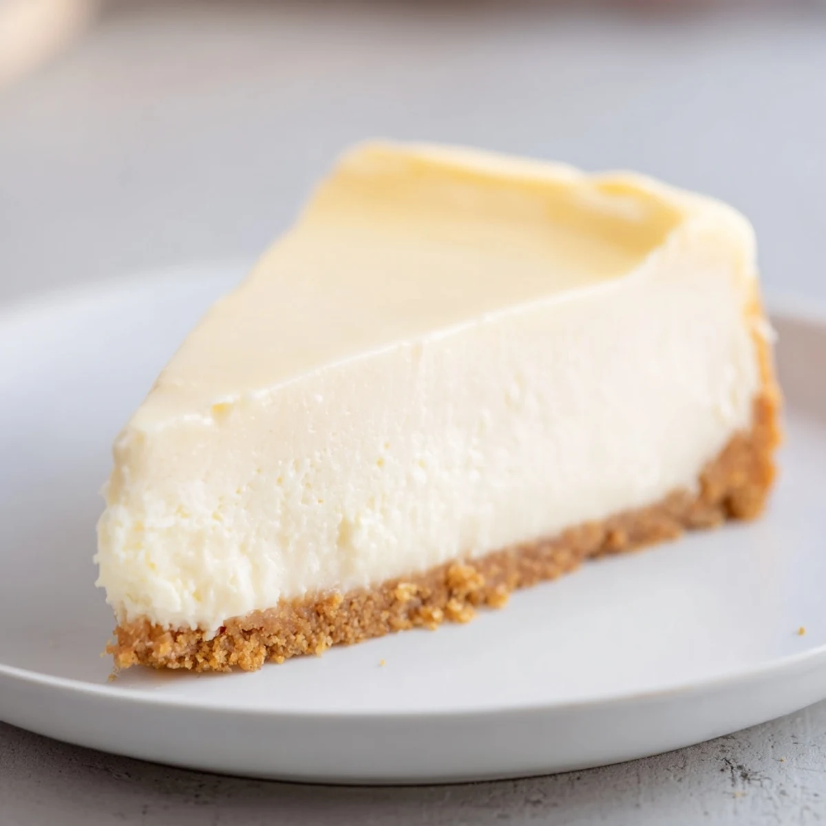A close-up view of a Rich Greek Yogurt Cheesecake with a graham cracker crust and a dollop of whipped cream.