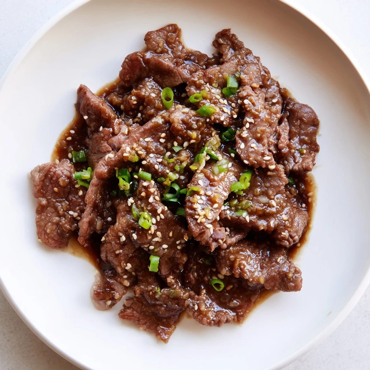 Slices of Ultimate Slow Cooker Mongolian Beef glisten with a savory-sweet sauce, garnished with green onions and sesame seeds.