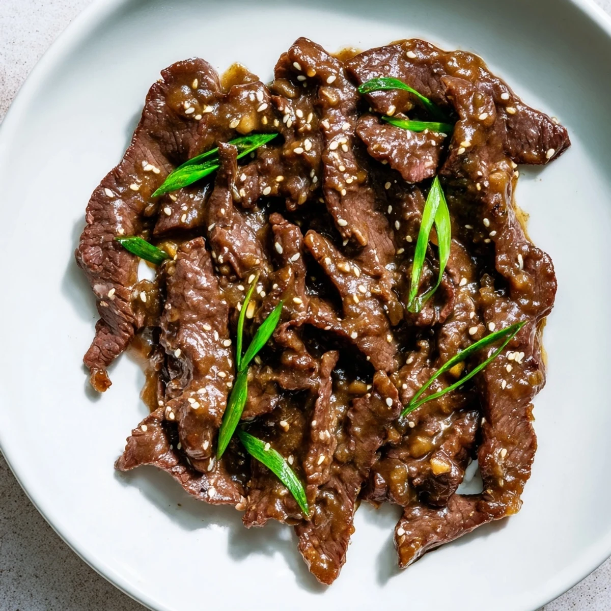 Tender beef strips from Ultimate Slow Cooker Mongolian Beef sit beside chopsticks and bright green onions on a plate.