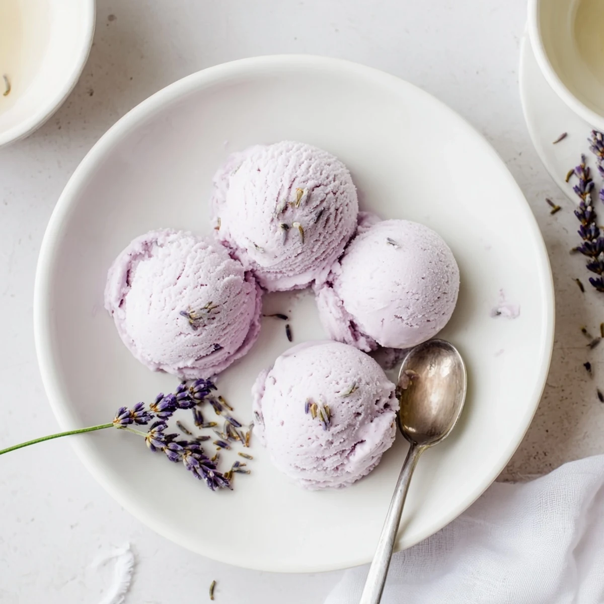 Creamy scoops of Lavender Ice Cream in a rustic bowl, topped with edible purple flowers and fresh berries.