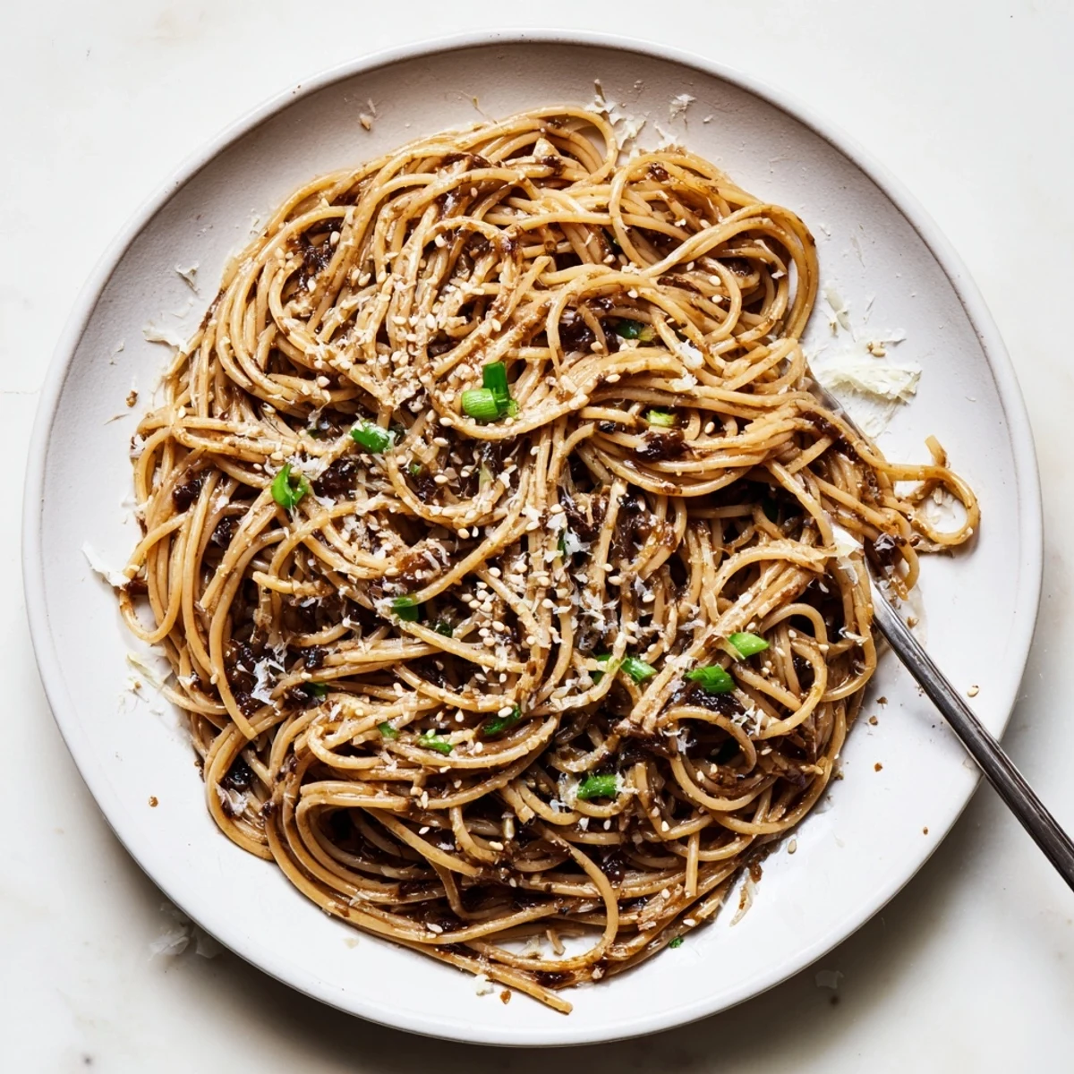 Steaming Garlic Noodles served hot as a savory main course, garnished with green onions and a sprinkle of Parmesan next to chopsticks.