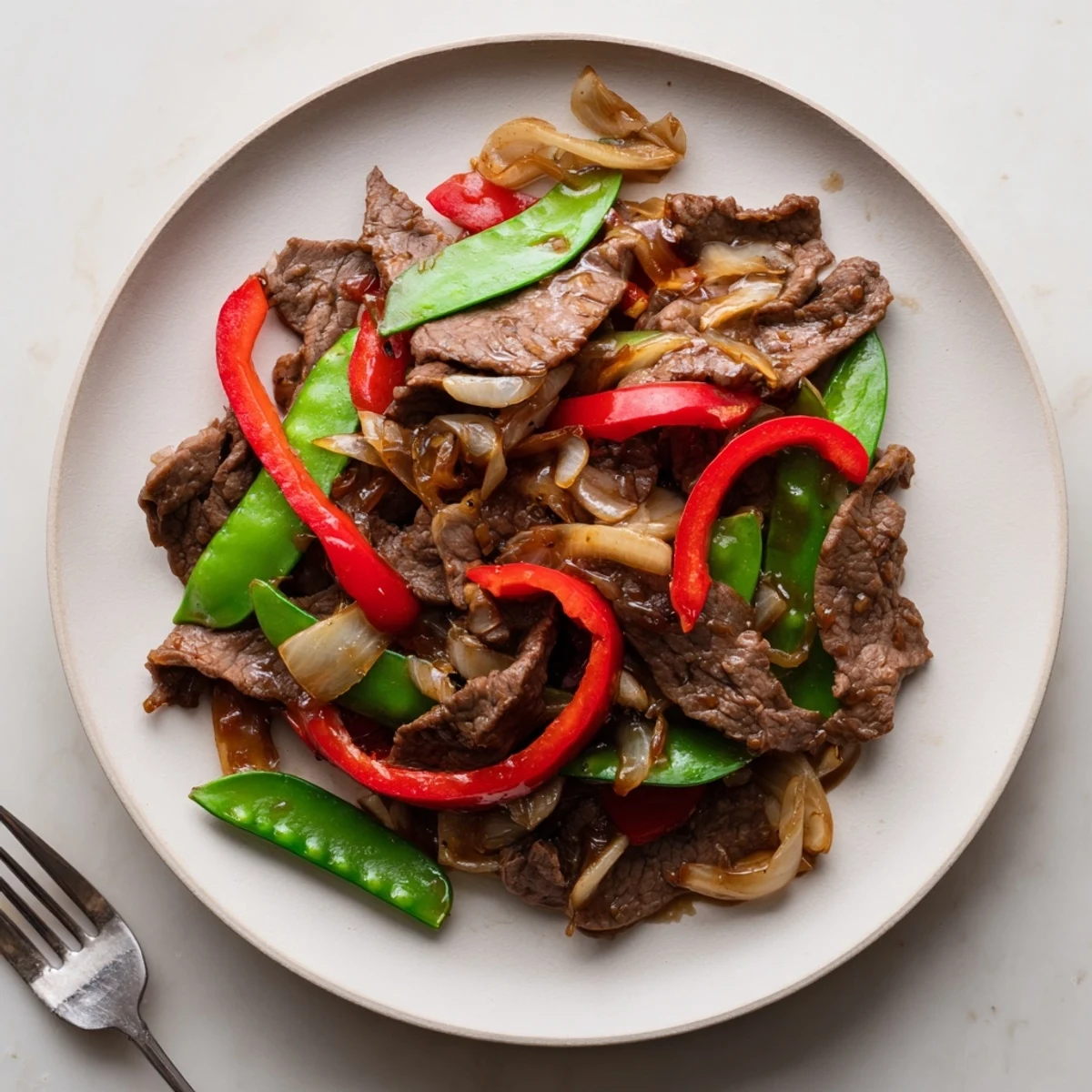 A close-up of Beef With Oyster Sauce served over steamed jasmine rice with bright red bell peppers and fresh green snow peas.