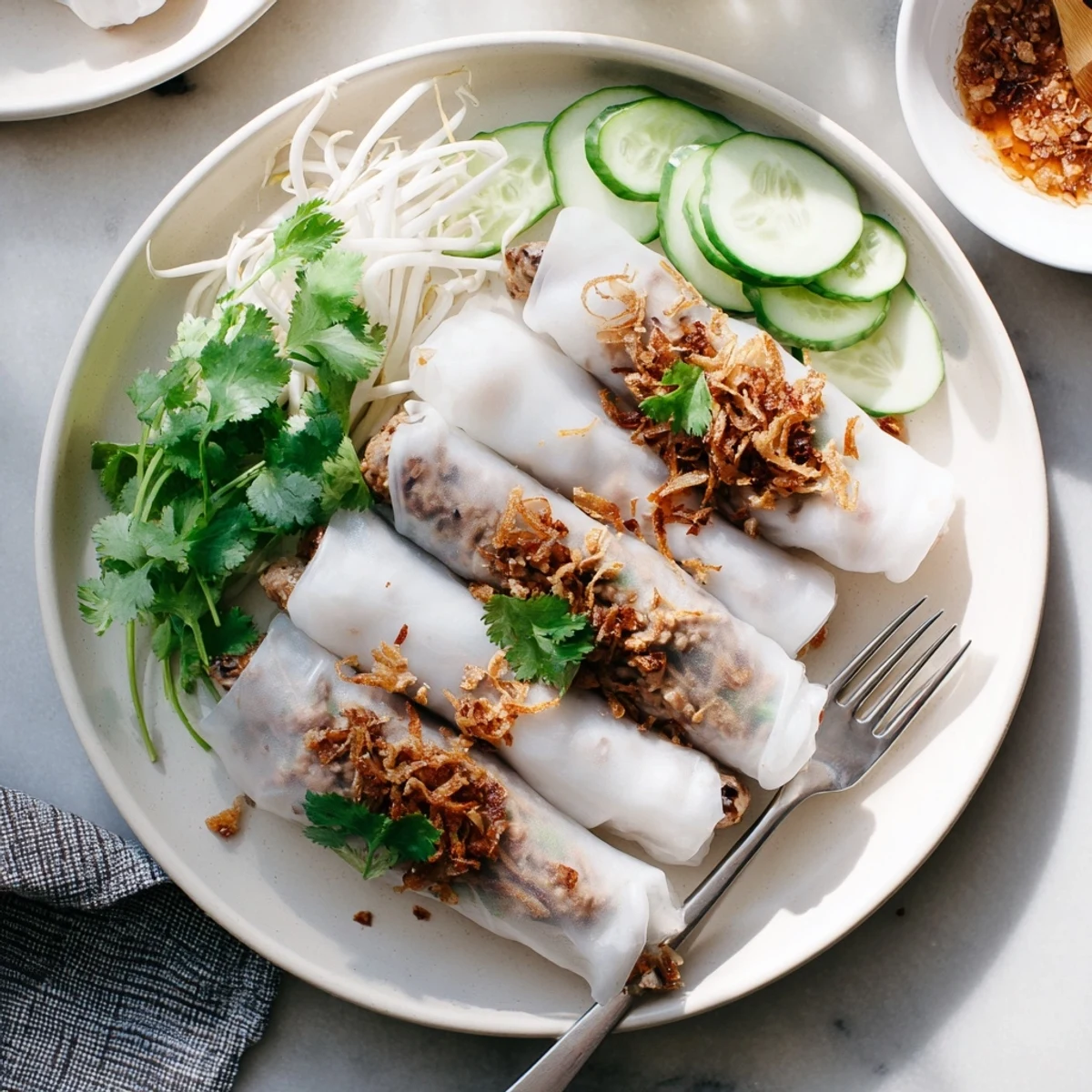 A platter of delicate Banh Cuon with fresh cilantro, bean sprouts, and a side of tangy Vietnamese dipping sauce ready to serve.