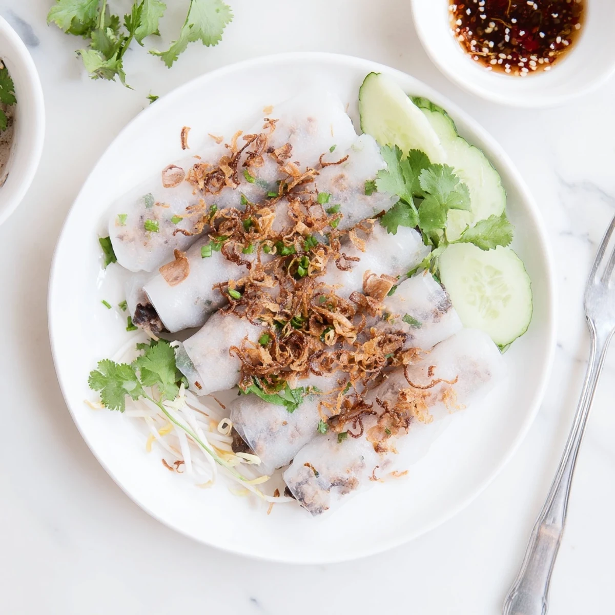 Vietnamese Banh Cuon rolls steamed to silky perfection, filled with seasoned pork and mushrooms, garnished with herbs and sliced cucumbers.