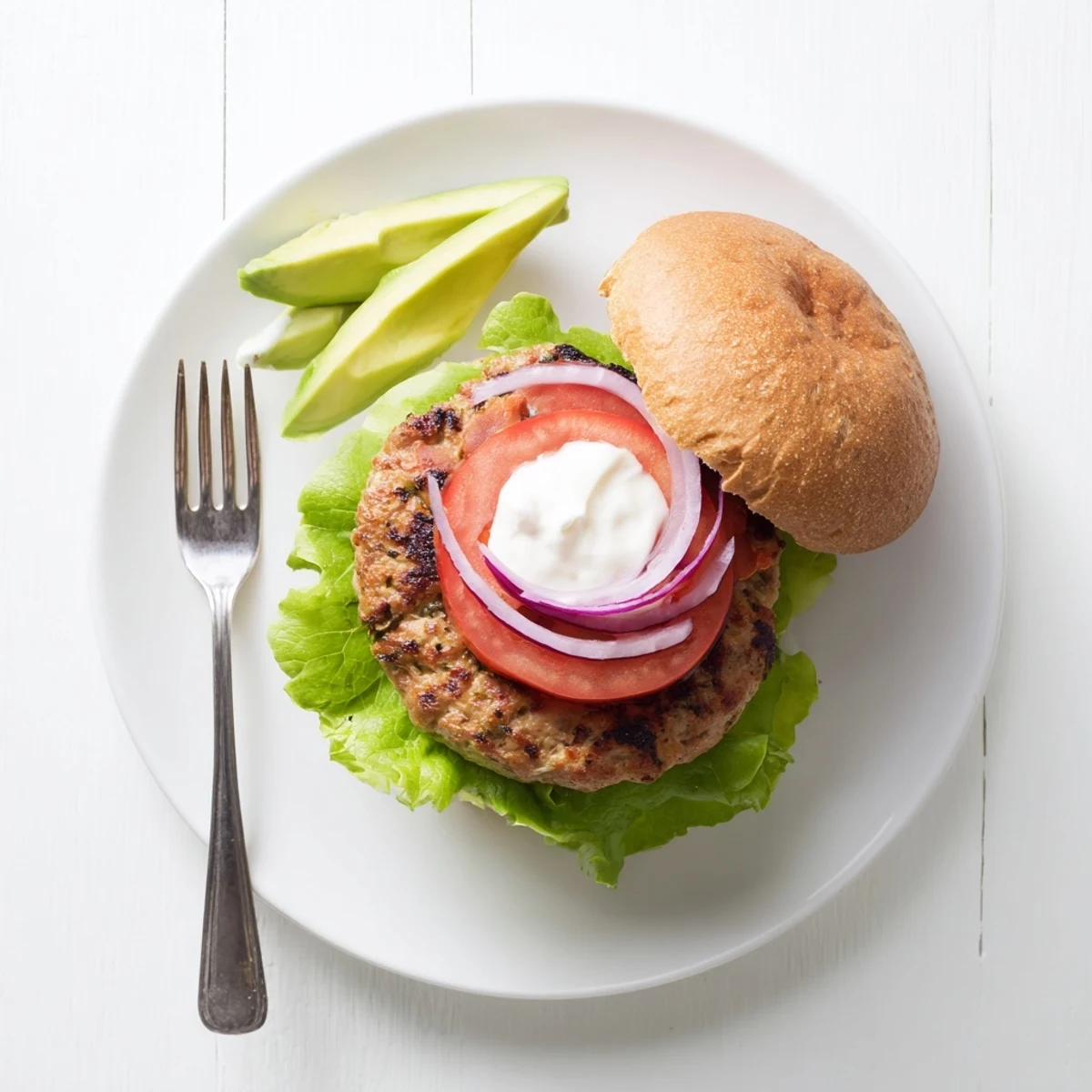 Juicy healthy high protein burger featuring lean ground turkey patty topped with crisp vegetables, sliced avocado, and red onion on a bakery-style bun