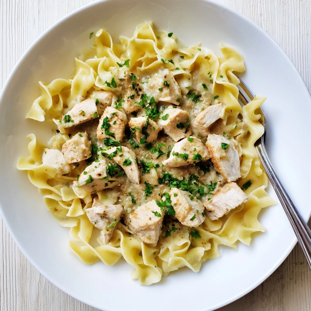 Tender one pan chicken with buttered noodles garnished with fresh parsley and parmesan