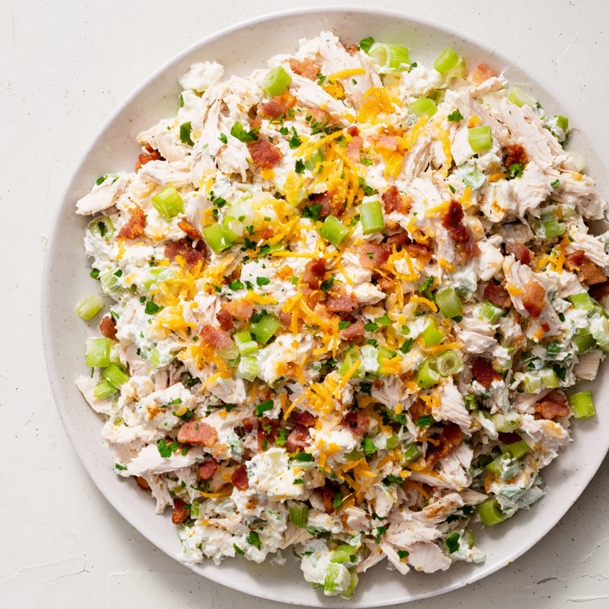 Creamy low carb jalapeno popper cottage cheese chicken salad topped with crispy bacon and fresh diced jalapeños in a white serving bowl