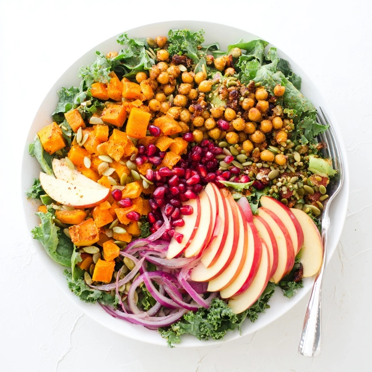 Golden roasted chickpea fall salad with butternut squash, crisp apple slices, and vibrant pomegranate seeds arranged on a bed of mixed greens
