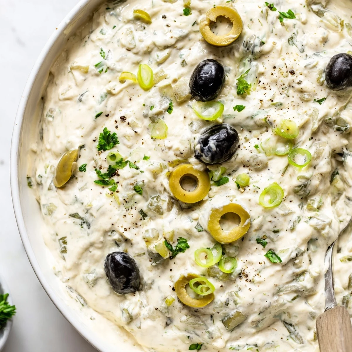 Cream cheese olive dip served in a white bowl with scattered green and black olives on top, garnished with fresh parsley and green onions