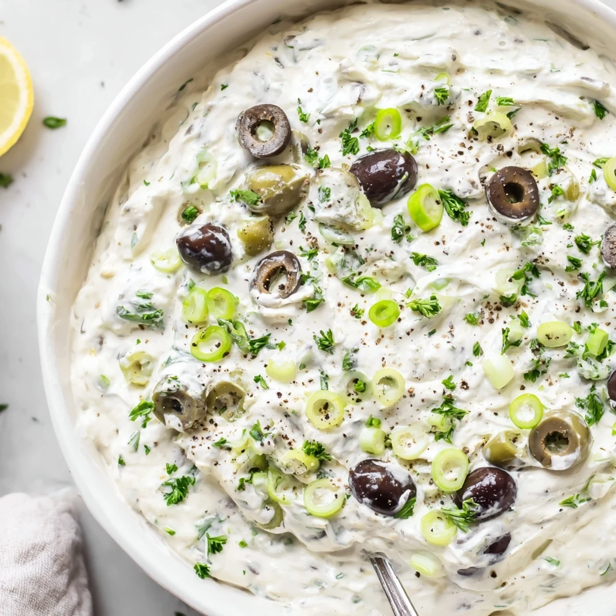 Spoonful of rich cream cheese olive dip showcasing the chopped green and black olives throughout the smooth, tangy white mixture