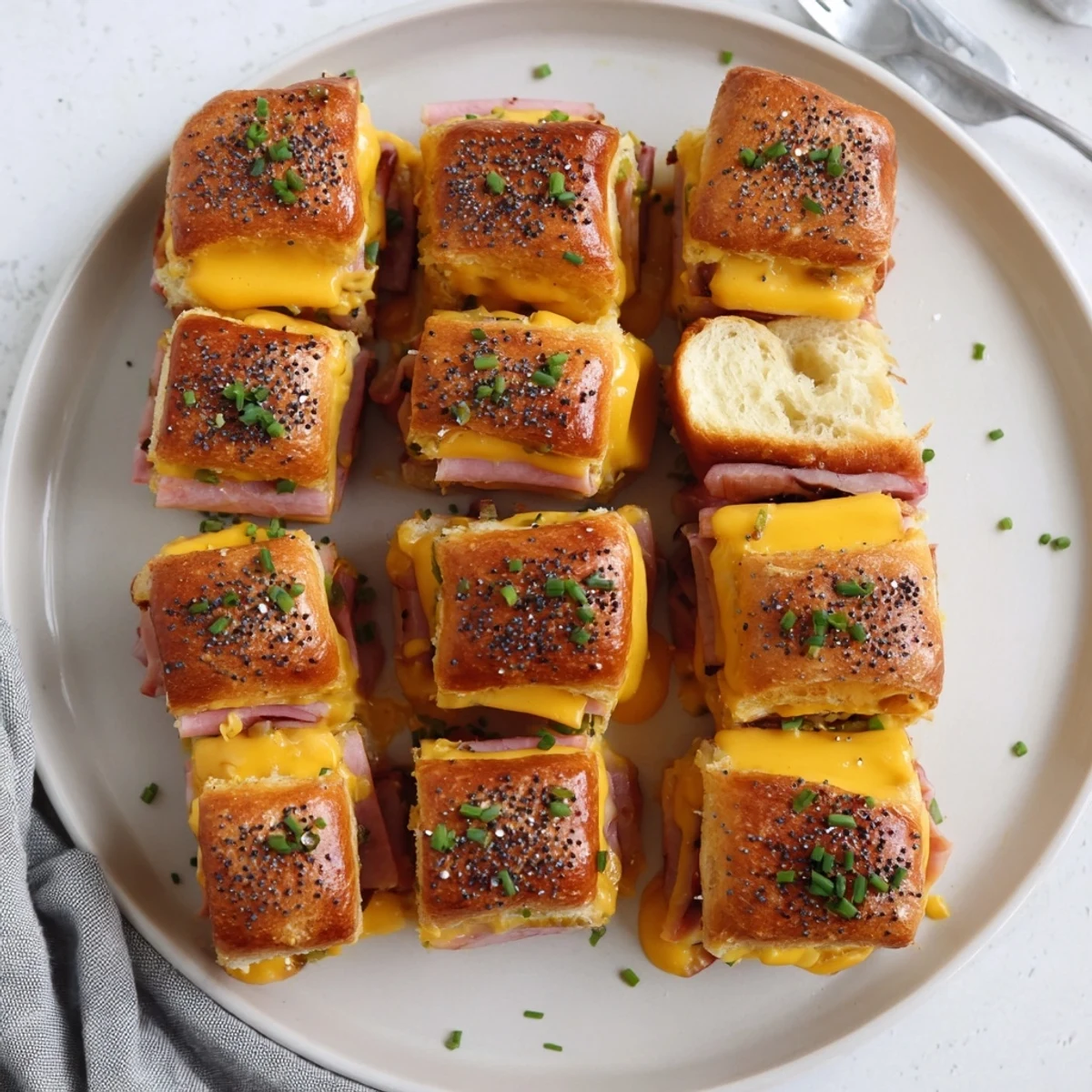 Golden mini Hawaiian roll sliders stacked with melted cheddar and savory ham on a wooden board