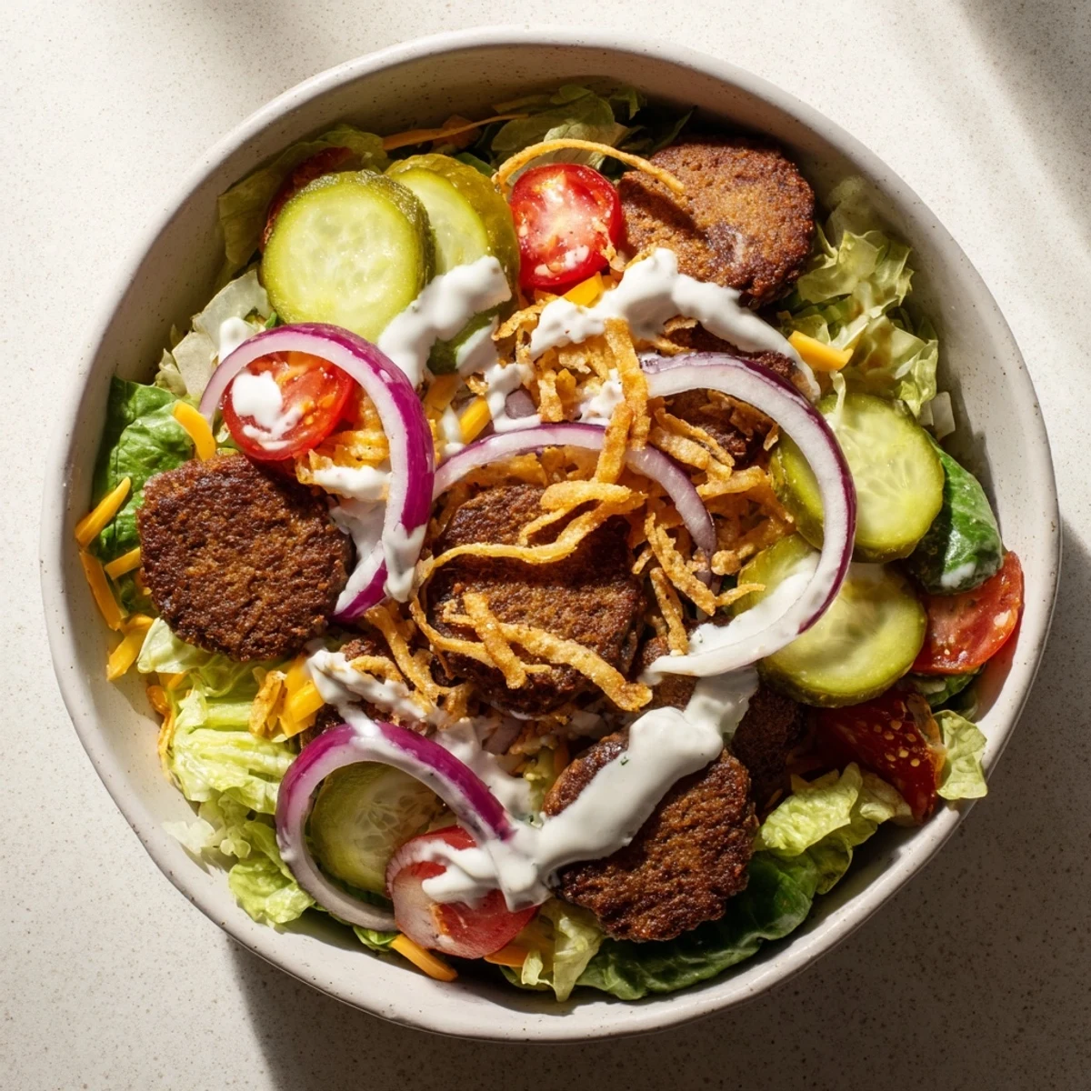 Deconstructed burger bowl with crispy patties, mixed salad greens, tomatoes, pickles, and fried onion toppings