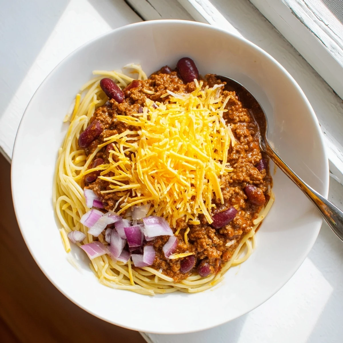 Hearty Cincinnati Chili serving featuring spiced meat sauce over pasta topped with shredded cheese