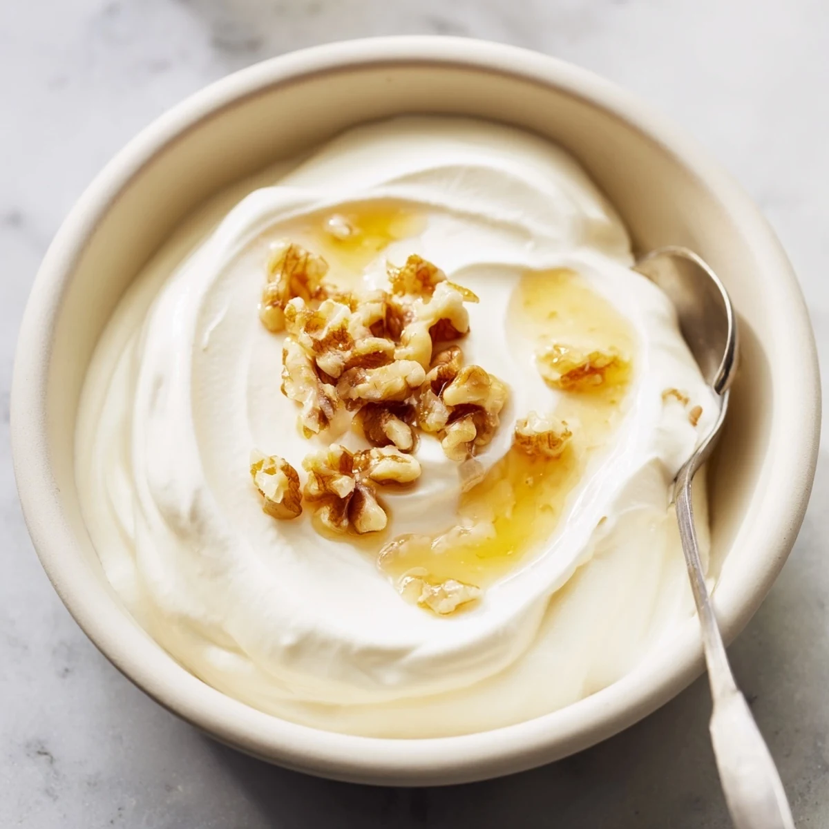 Golden bowl of tangy Greek yogurt served with walnuts and sweet maple syrup