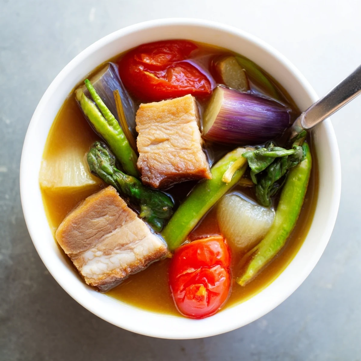 Steaming bowl of Filipino Sinigang with tender pork chunks and vibrant vegetables in tangy tamarind broth
