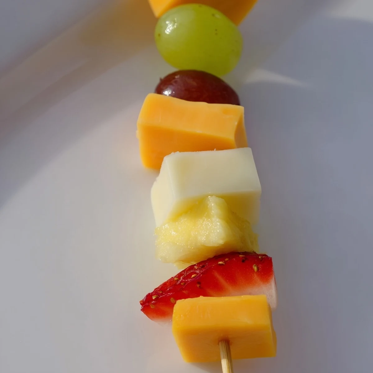 Colorful fruit and cheese kabobs arranged on a platter with grapes strawberries pineapple and cubed cheddar
