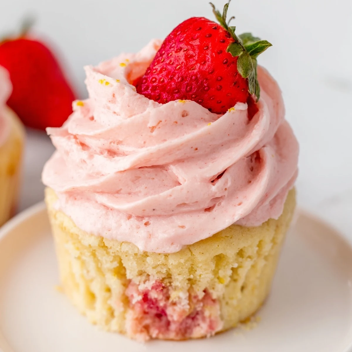 Golden strawberry lemonade cupcakes crowned with swirled pink buttercream on a rustic plate