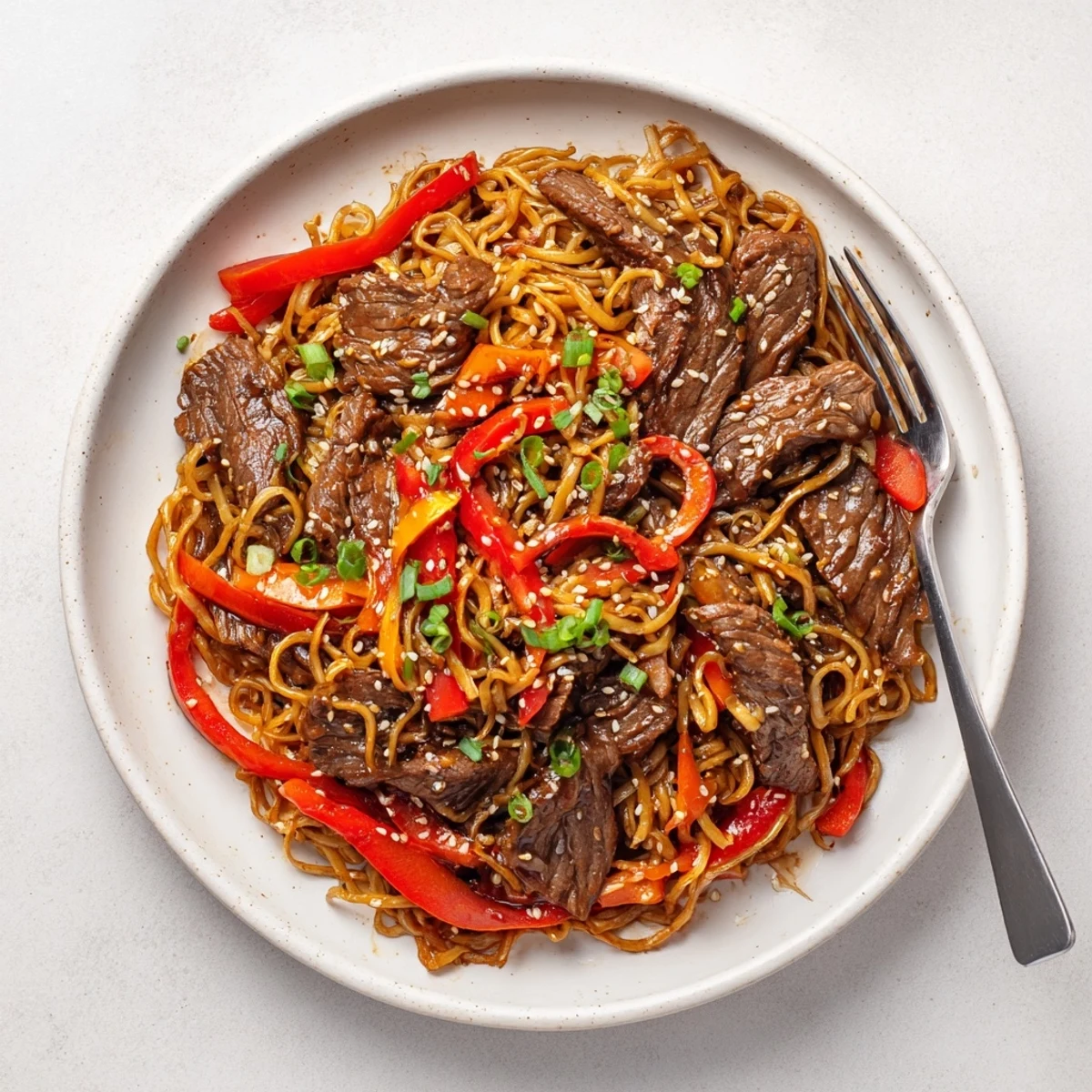 Family-style Sticky Beef Noodles steaming on plate, sesame seeds and cilantro