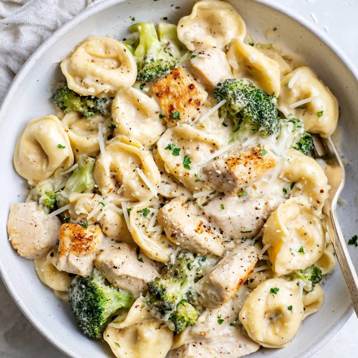 Bowl of Creamy Garlic Parmesan Tortellini Chicken Broccoli Recipe topped with parsley.