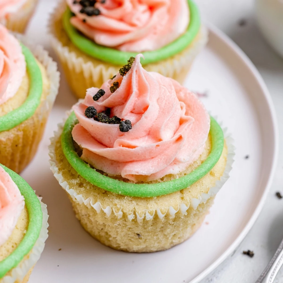 Watermelon Cupcakes with glossy pink frosting and chocolate seeds on plate