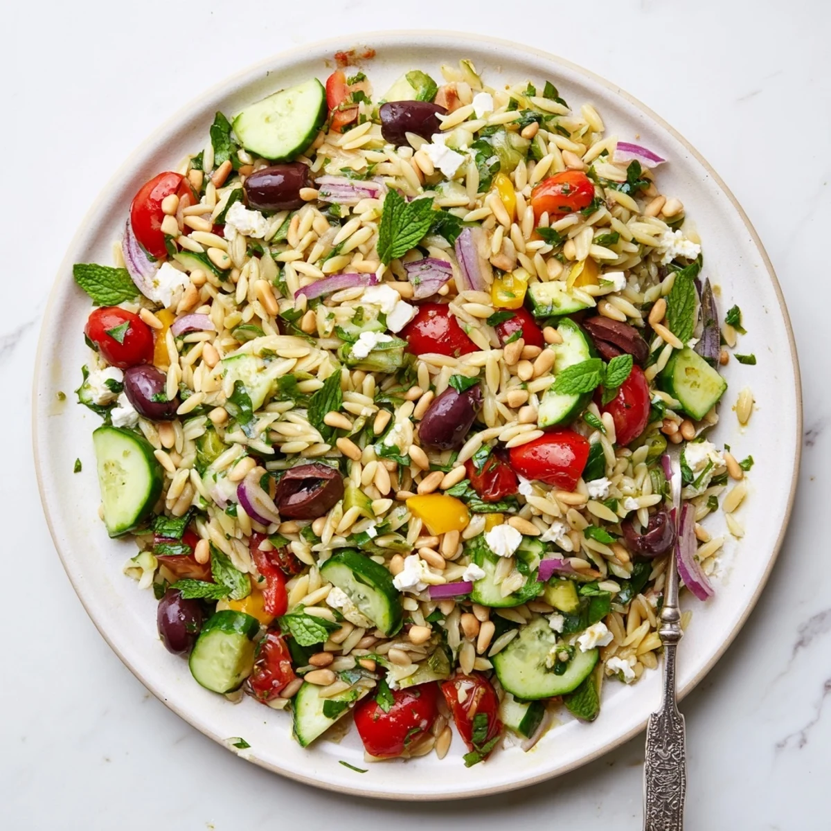 Bowl of Mediterranean orzo power salad featuring cherry tomatoes, cucumber, olives, and crumbled feta