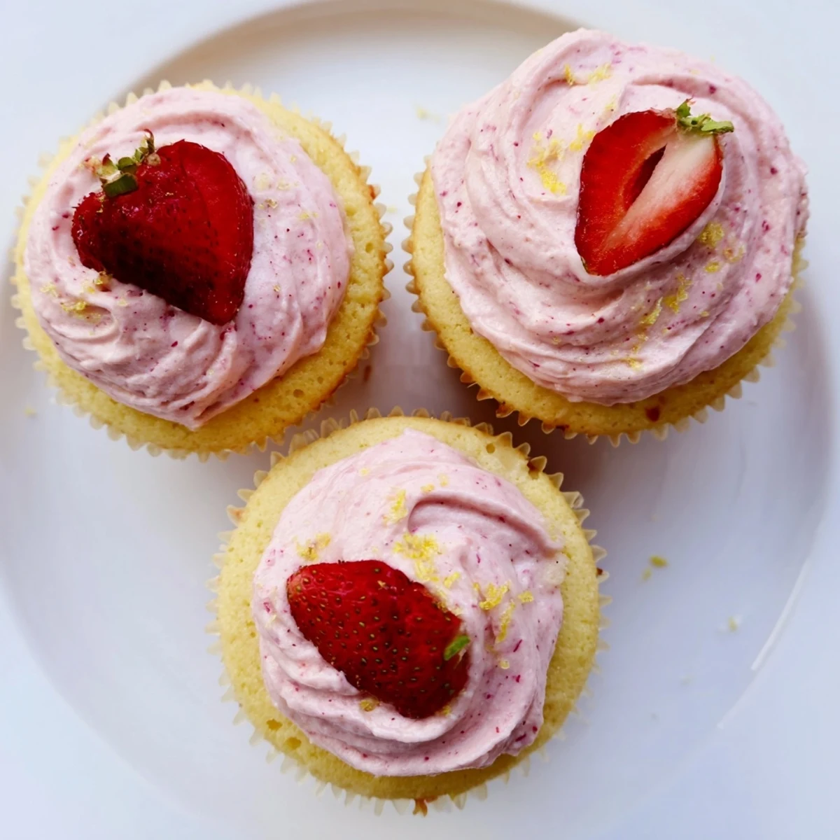 Golden lemon cupcakes swirled with creamy pink strawberry frosting and garnished with fresh lemon zest