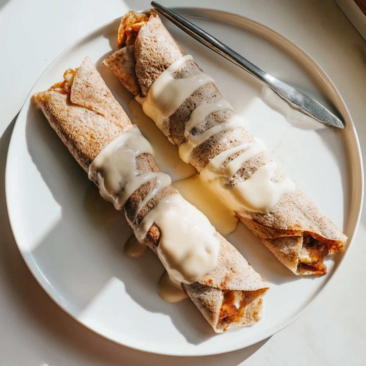 Cinnamon Roll Protein Crepes drizzled with cream cheese glaze on a warm plate