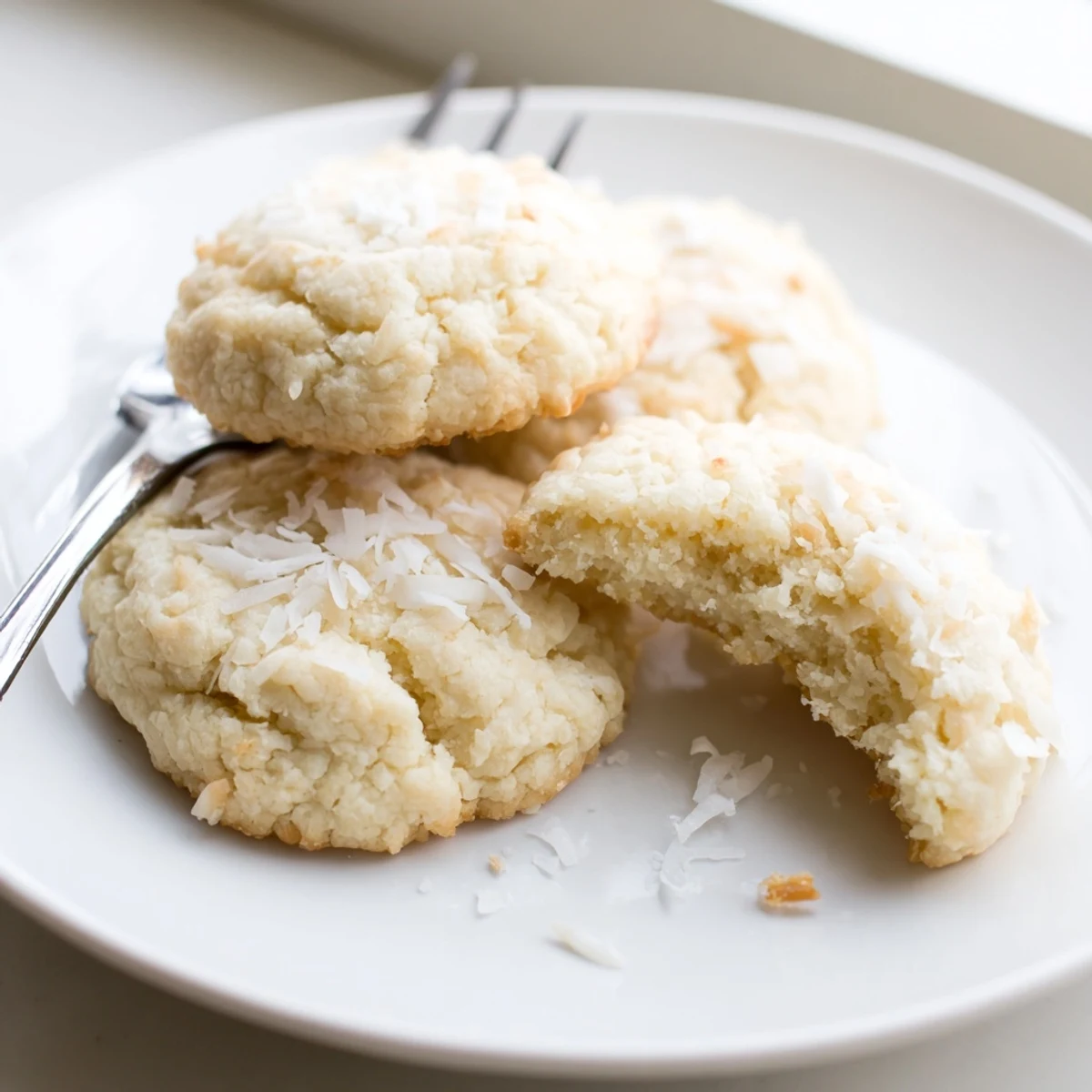 Warm coconut cookies with lightly browned edges stacked beside a glass of milk